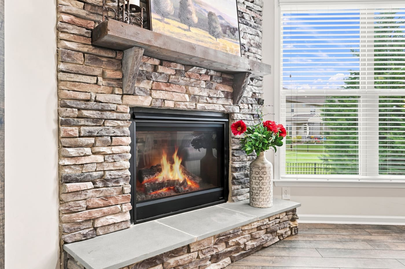 A close view of the stacked-stone fireplace, fire lit, with a timber mantel and a raised hearth.