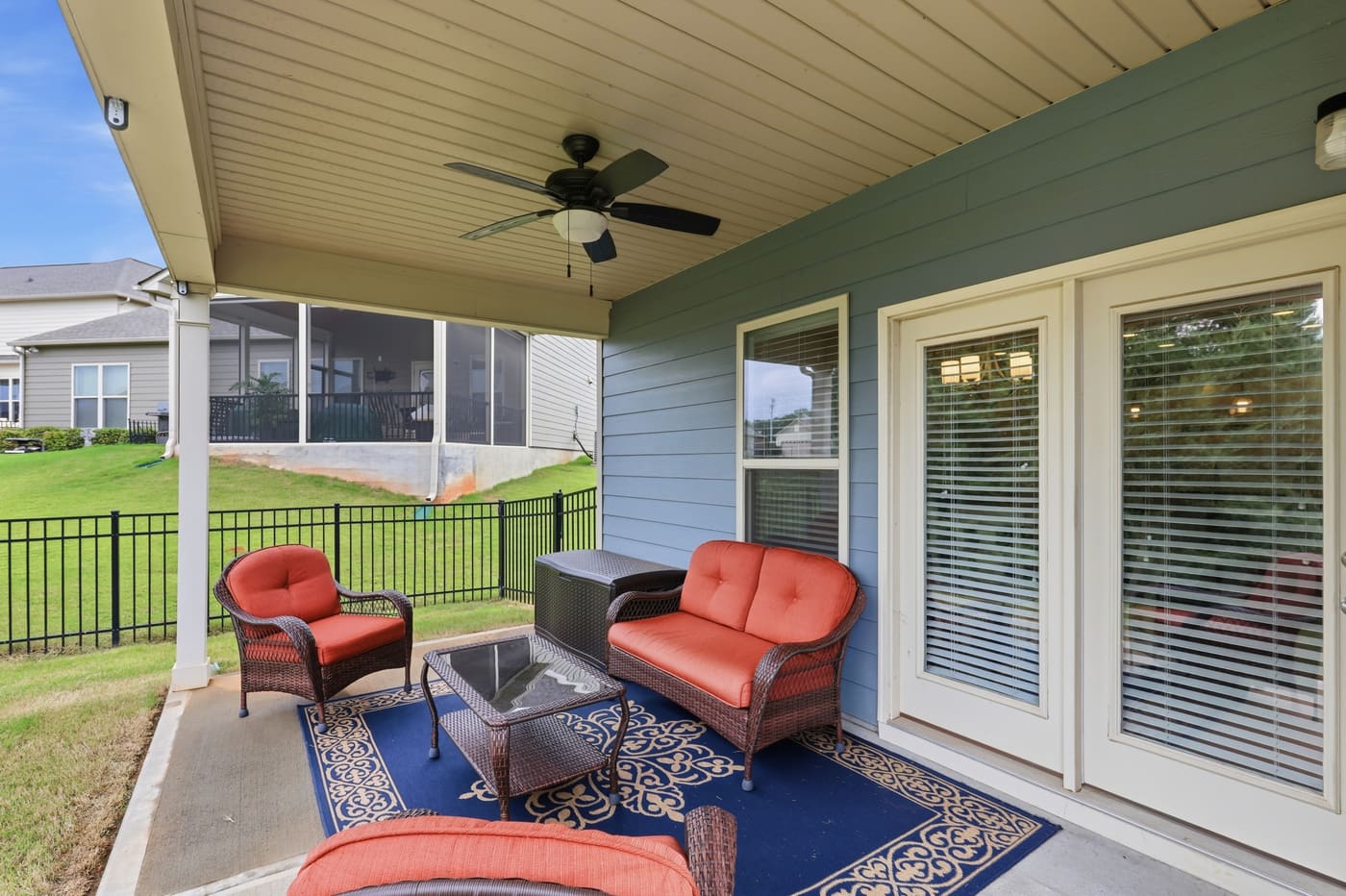 The covered rear porch furnished with wicker chairs, looking out over the fenced lawn.