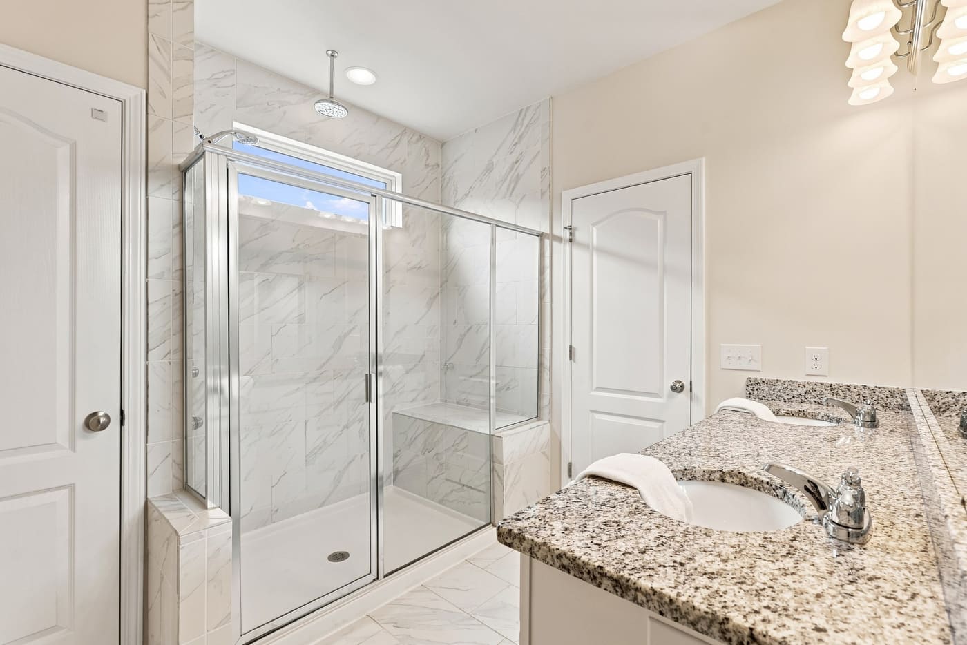 The tiled, glass-enclosed shower in the primary bath beside the granite vanity.